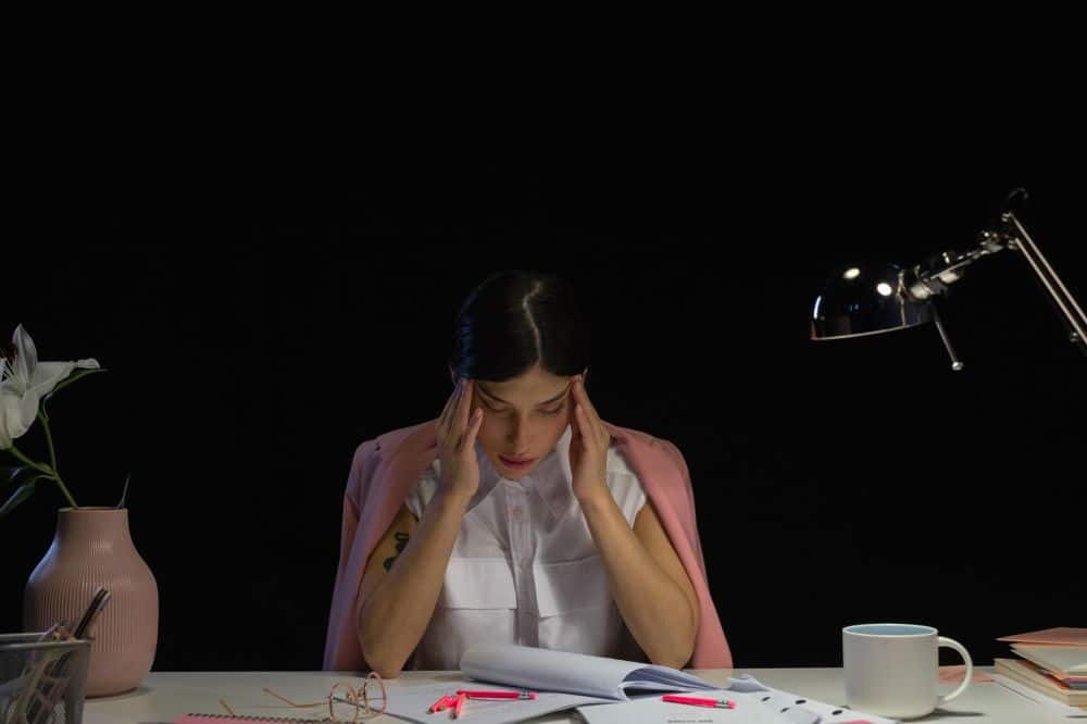 Woman pressing temples at desk showing tension headache and chronic migraine symptoms